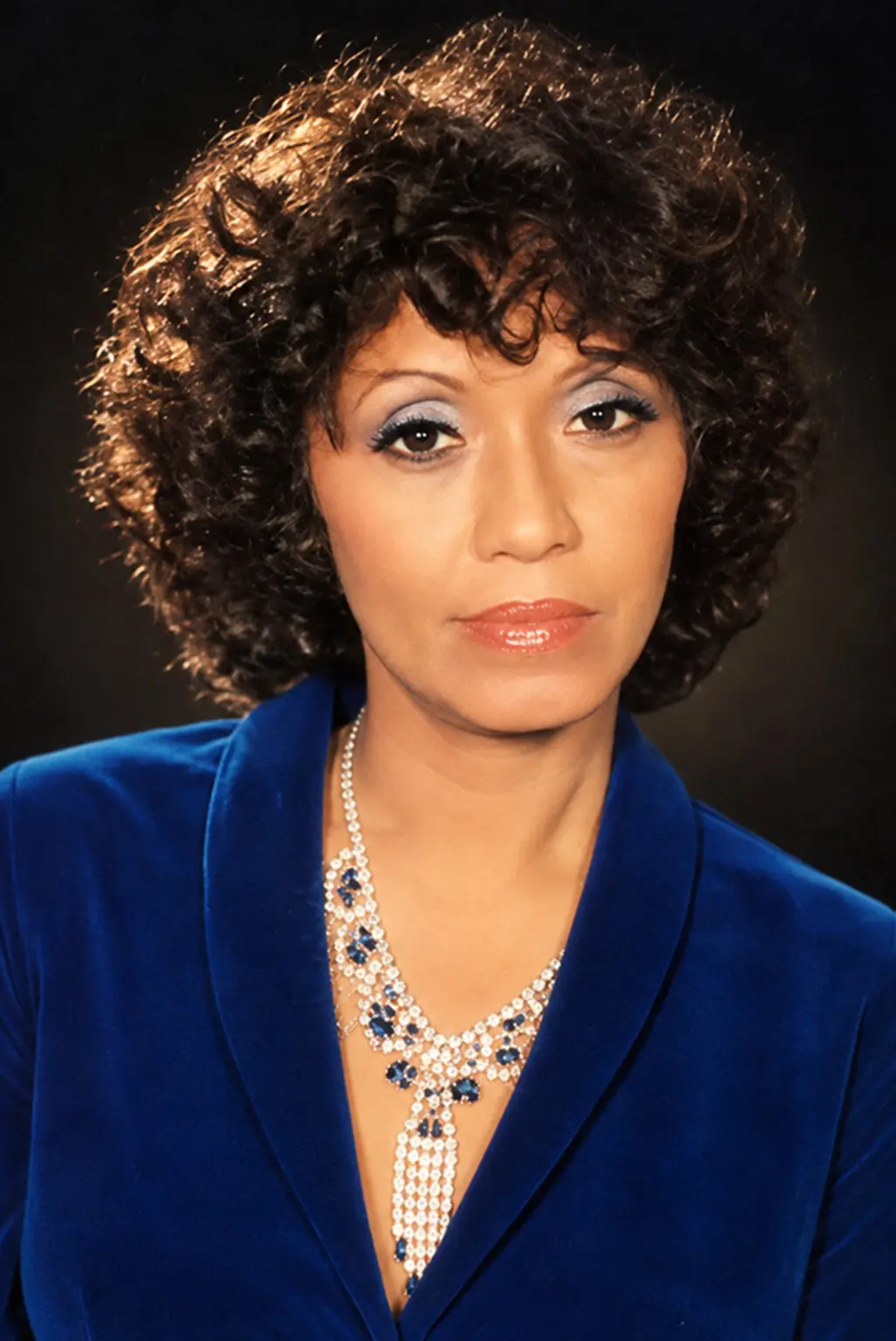 Colour studio portrait of Saloma in a blue velvet jacket and jewelled necklace